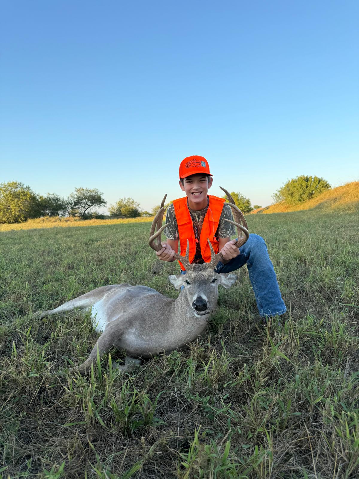 A smiling young hunter with a harvested whitetail buck in a grassy field